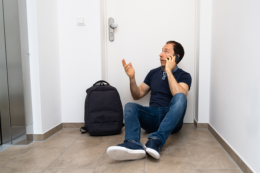 A man outside of his apartment on the phone with a locksmith because he has been locked out.