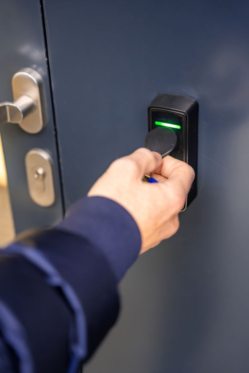 Close up view of a person using an electric key fob to access a building via a proximity reader mounted by the entrance